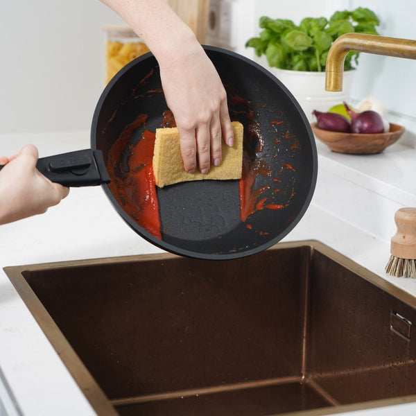 Hand spült CuliStack Antihaftpfanne mit Tomatensoße per Hand mit weichem Schwamm in moderner Küche